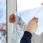 Professional worker tinting window with foil indoors, focus on film, closeup